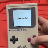 a person is holding a nintendo gameboy in front of a red box